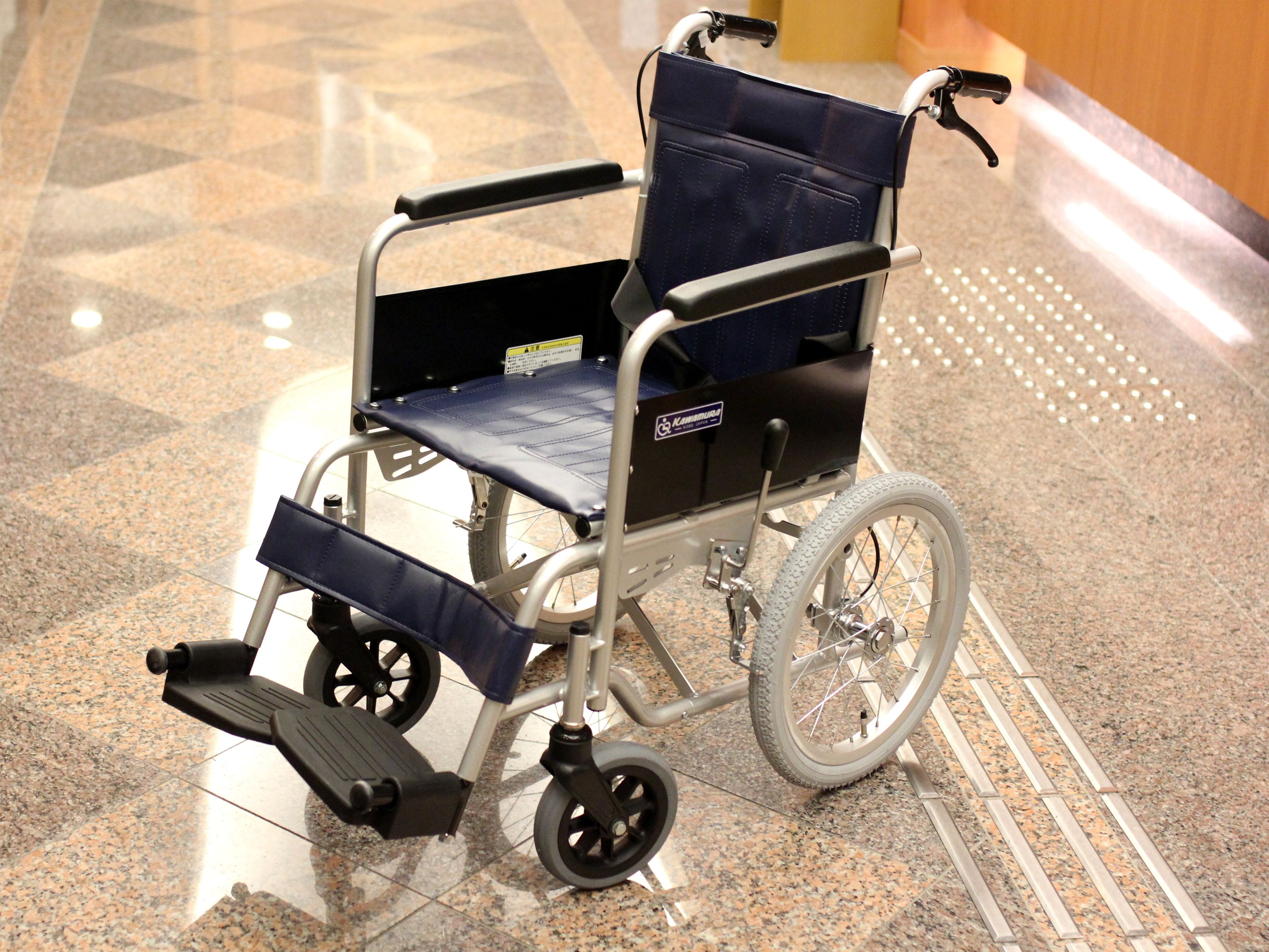 Een rolstoel met een blauwe zitting en rugleuning, een metalen frame en zwarte voetsteunen.