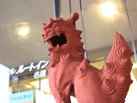 Una estatua de león rojo con diseños intrincados, ubicada frente a un ventanal con un letrero que dice "COOLBIZ".