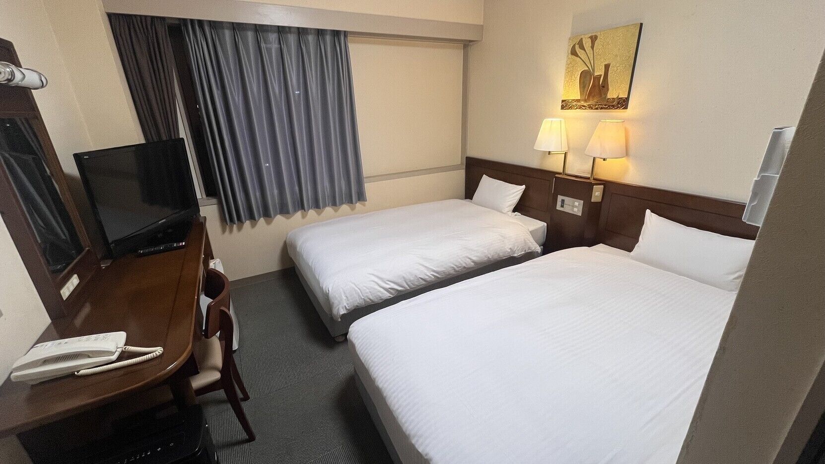 A hotel room with two beds, a desk with a telephone, a television, and a painting on the wall.