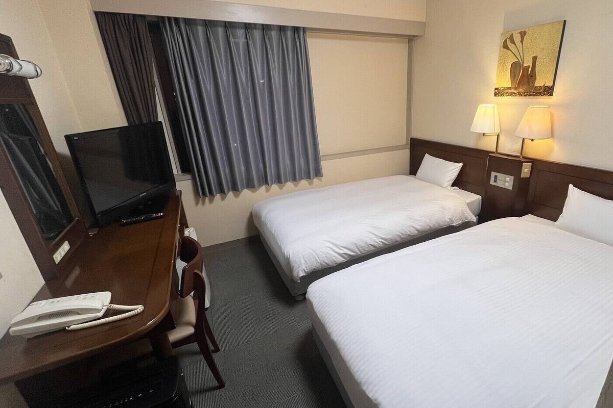 A hotel room with two beds, a desk with a telephone, a television, and a painting on the wall.