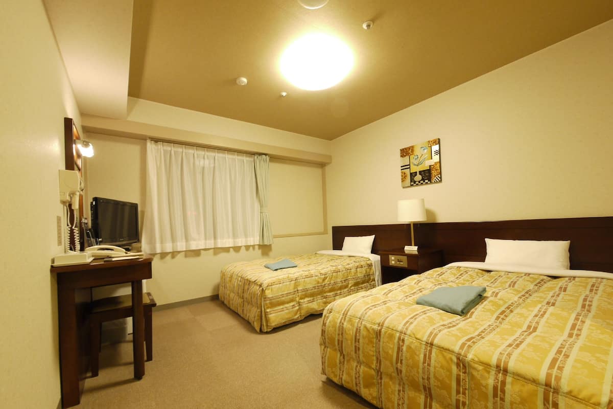 A hotel room with two beds, a desk with a telephone, and a window with curtains.