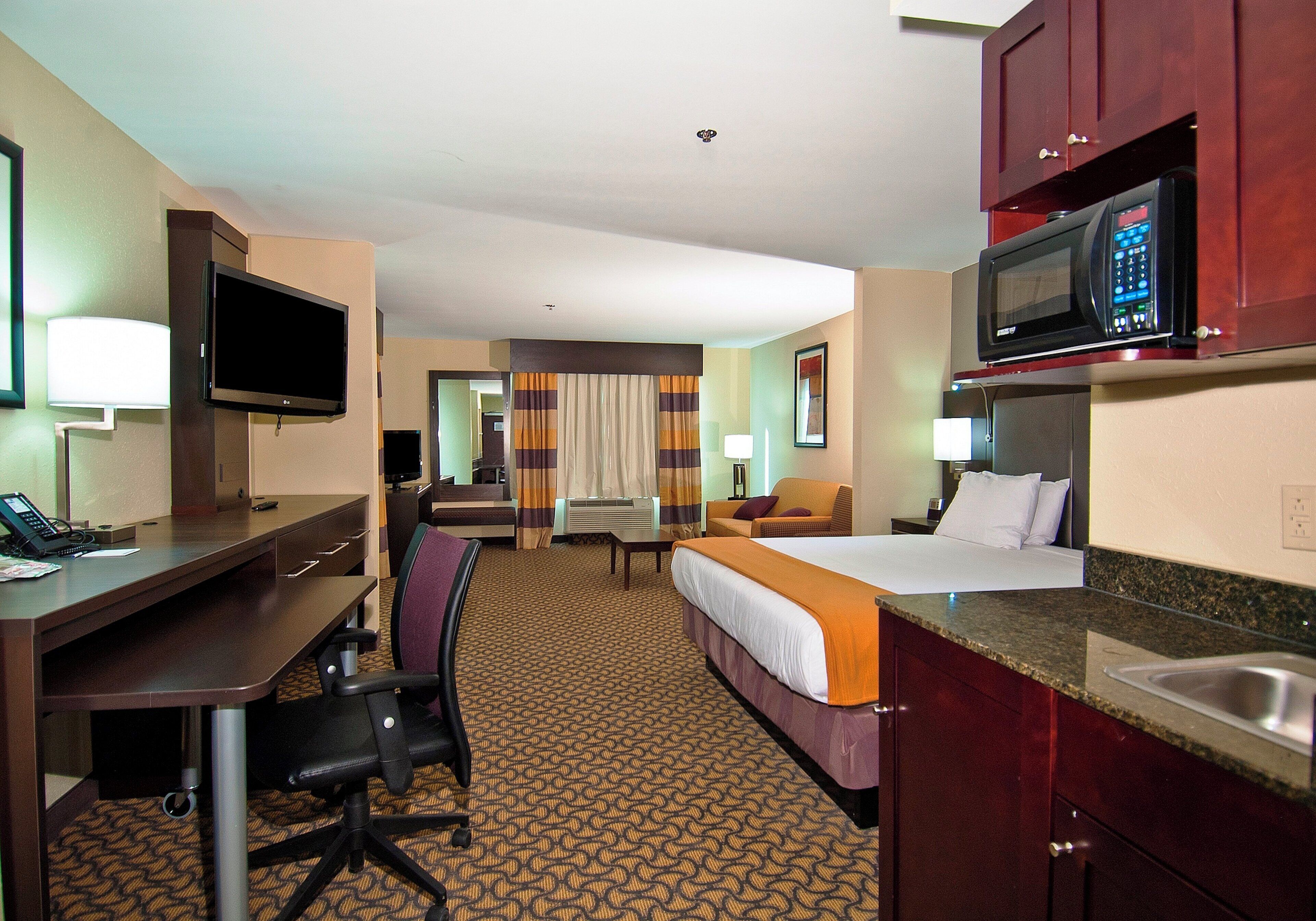 Habitación de hotel con cama, escritorio, silla, televisor, microondas y baño.