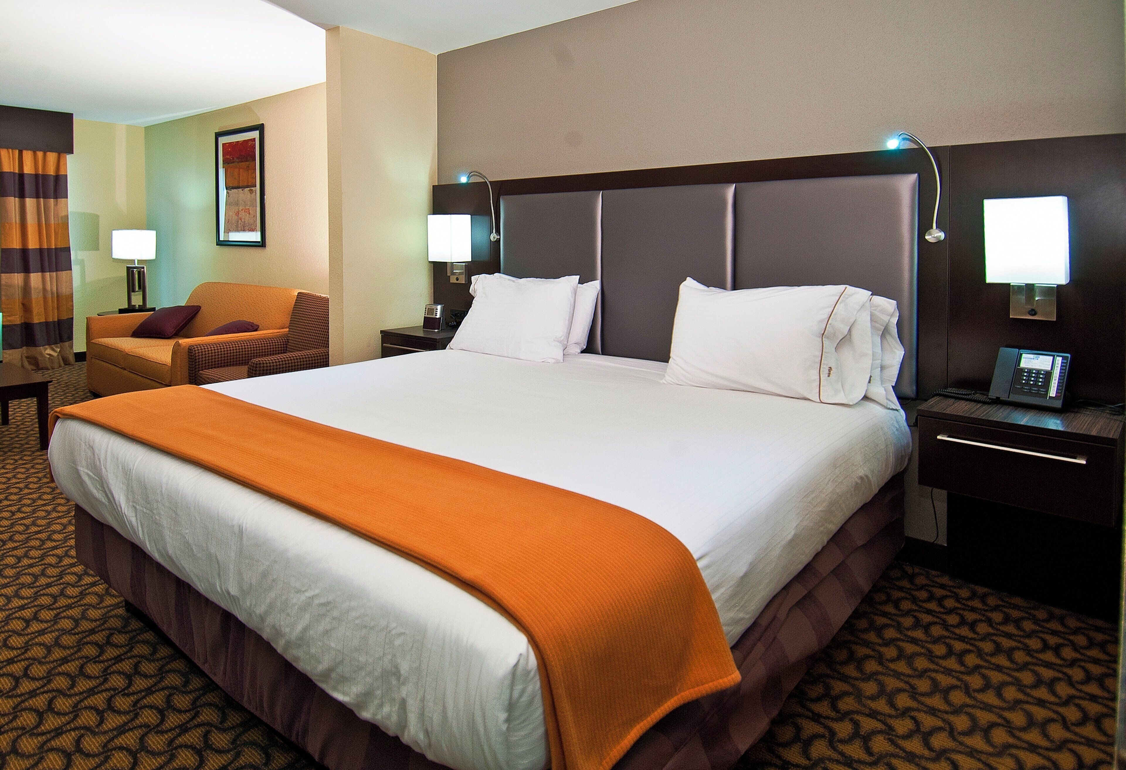 Una habitación de hotel con una cama grande, una silla, un escritorio y una mesita de noche con lámpara.