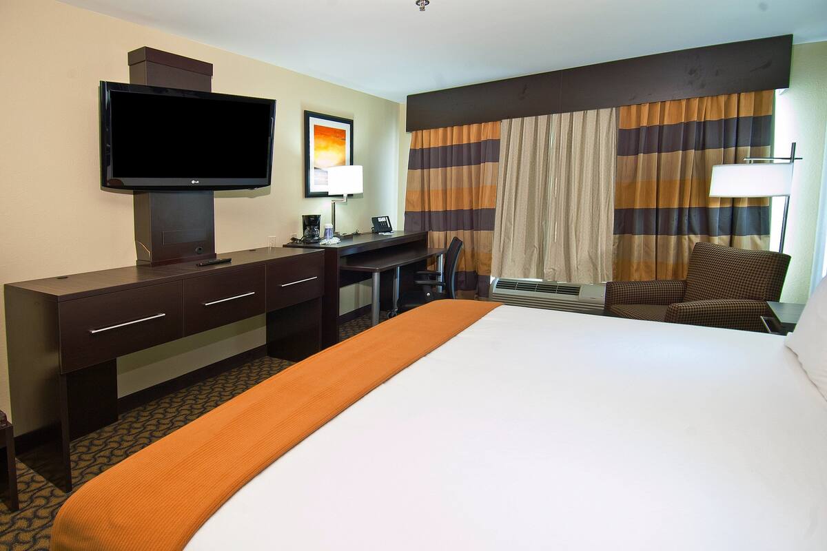 A hotel room with a bed, a desk, a television, a chair, and curtains.