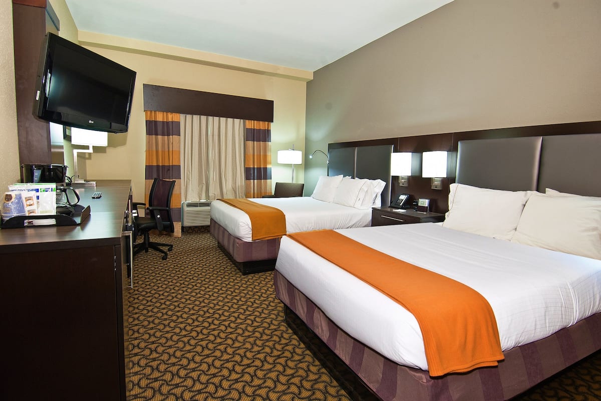 A hotel room with two beds, a desk with a computer, a flat-screen TV, and a window with curtains.