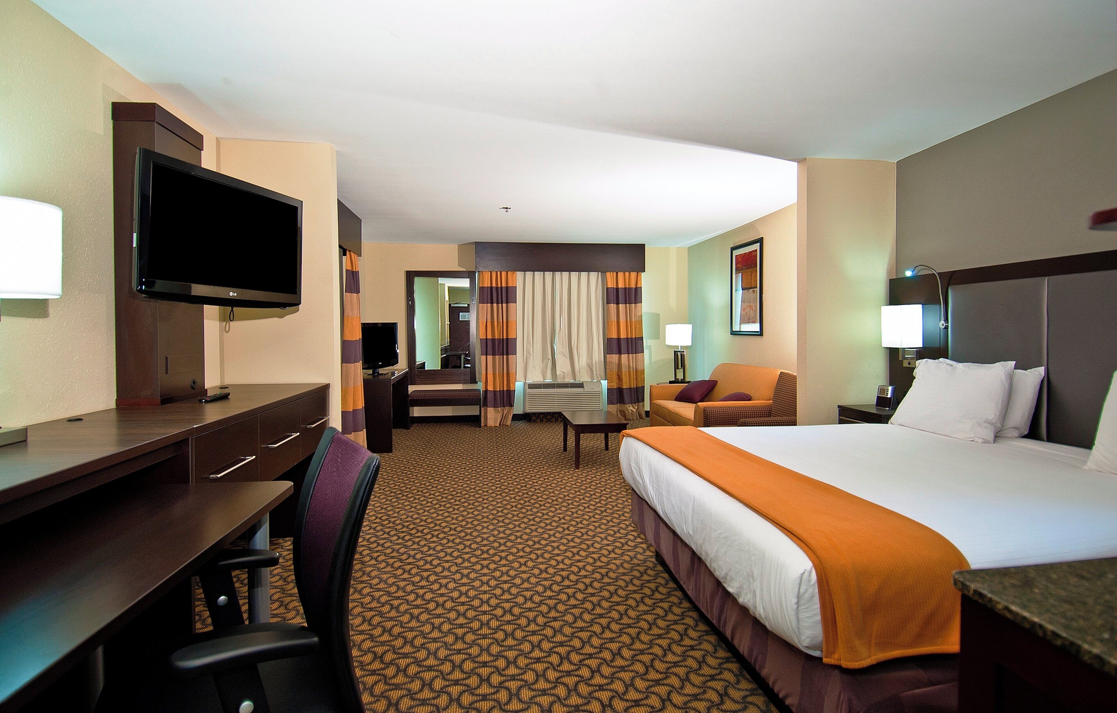 A hotel room with a bed, desk, chair, TV, and a view of the hallway.