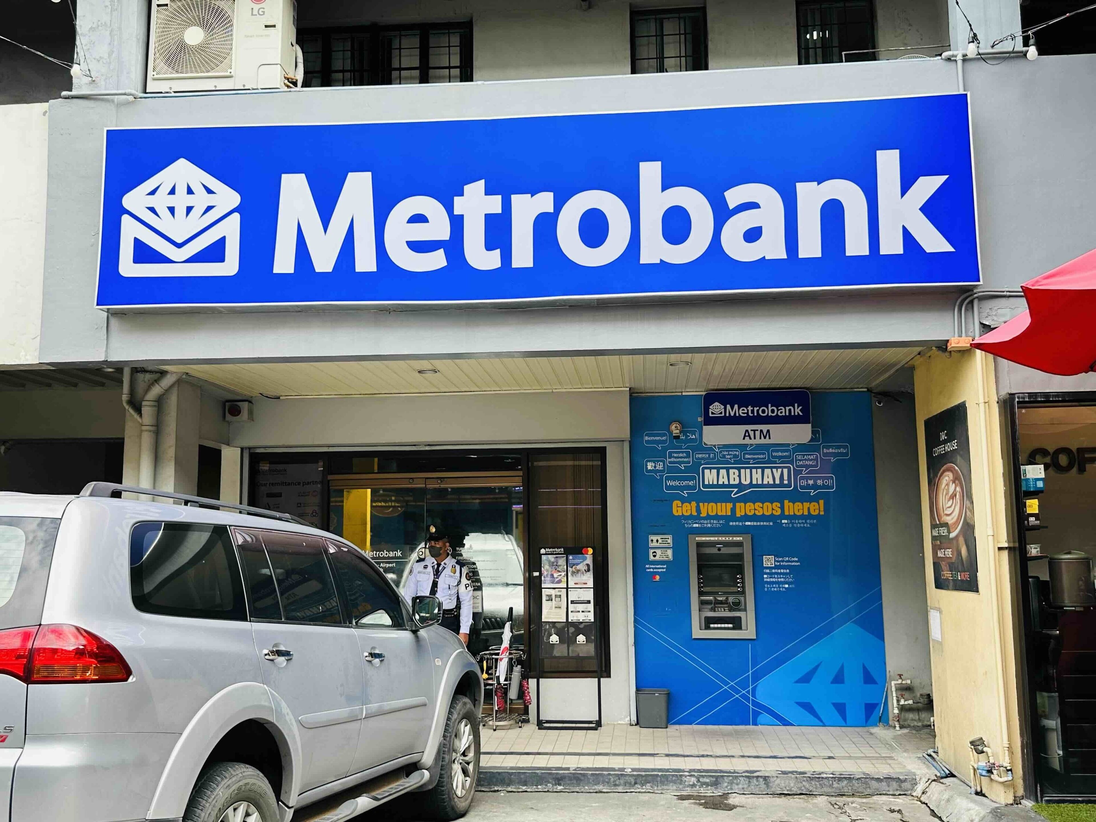 Un cajero automático de Metrobank con un letrero azul y una sombrilla roja cerca.