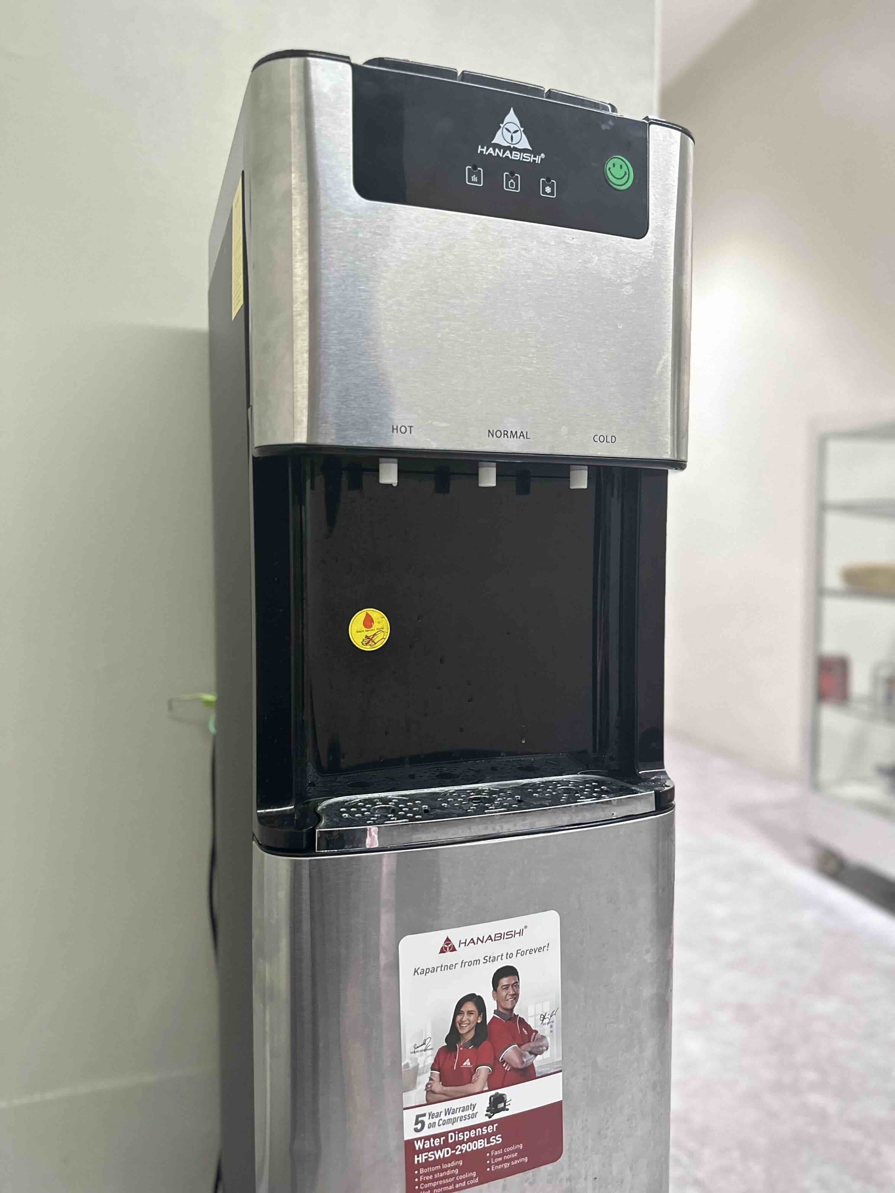 A stainless steel water dispenser with a control panel displaying temperature settings and a 5-year warranty sticker.