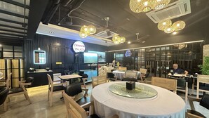 Interior de restaurante con mesas redondas, sillas y lámparas esféricas colgantes.