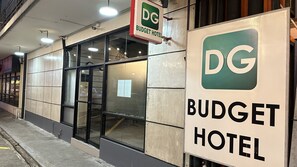 El exterior de un hotel económico con el logotipo de DG, un letrero que indica que es un hotel económico, y una entrada visible con puertas de vidrio.