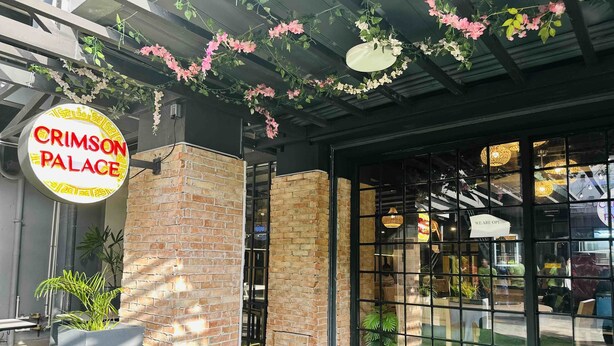 Un restaurante llamado 'CRIMSON PALACE' con fachada de ladrillo, ventanas grandes y decoración floral colgante.