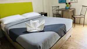 Una cama bien hecha con una disposición de toallas blancas, un cabecero verde y una pequeña mesa con sillas en una habitación de hotel.