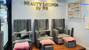 Un salón de belleza con tres sillones grises y un otomano rosa y mullido.