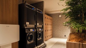 A laundry area with two stacked washing machines, wooden lockers, and a potted plant. - Hotel Keihan Sapporo (Sapporo)