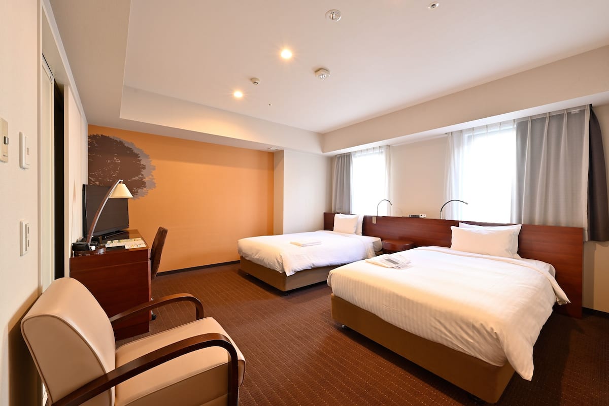 Una habitación de hotel con dos camas, un escritorio con lámpara y una silla.