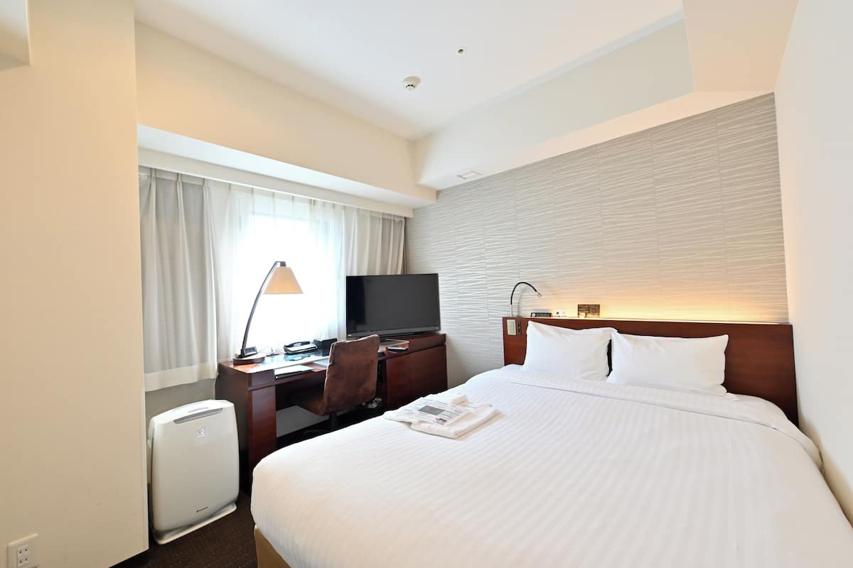 Habitación de hotel con cama, escritorio con computadora, televisor y calentador de pared.
