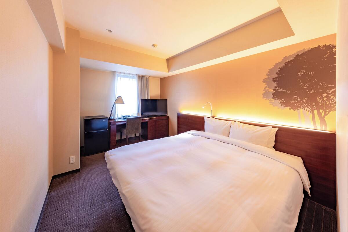 Una habitación de hotel con una cama grande, un escritorio con silla, un televisor y una lámpara de pared.