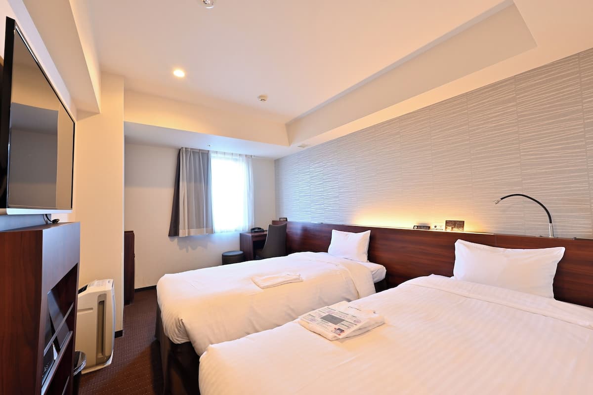Habitación de hotel con dos camas, televisión, escritorio y ventana con cortinas.