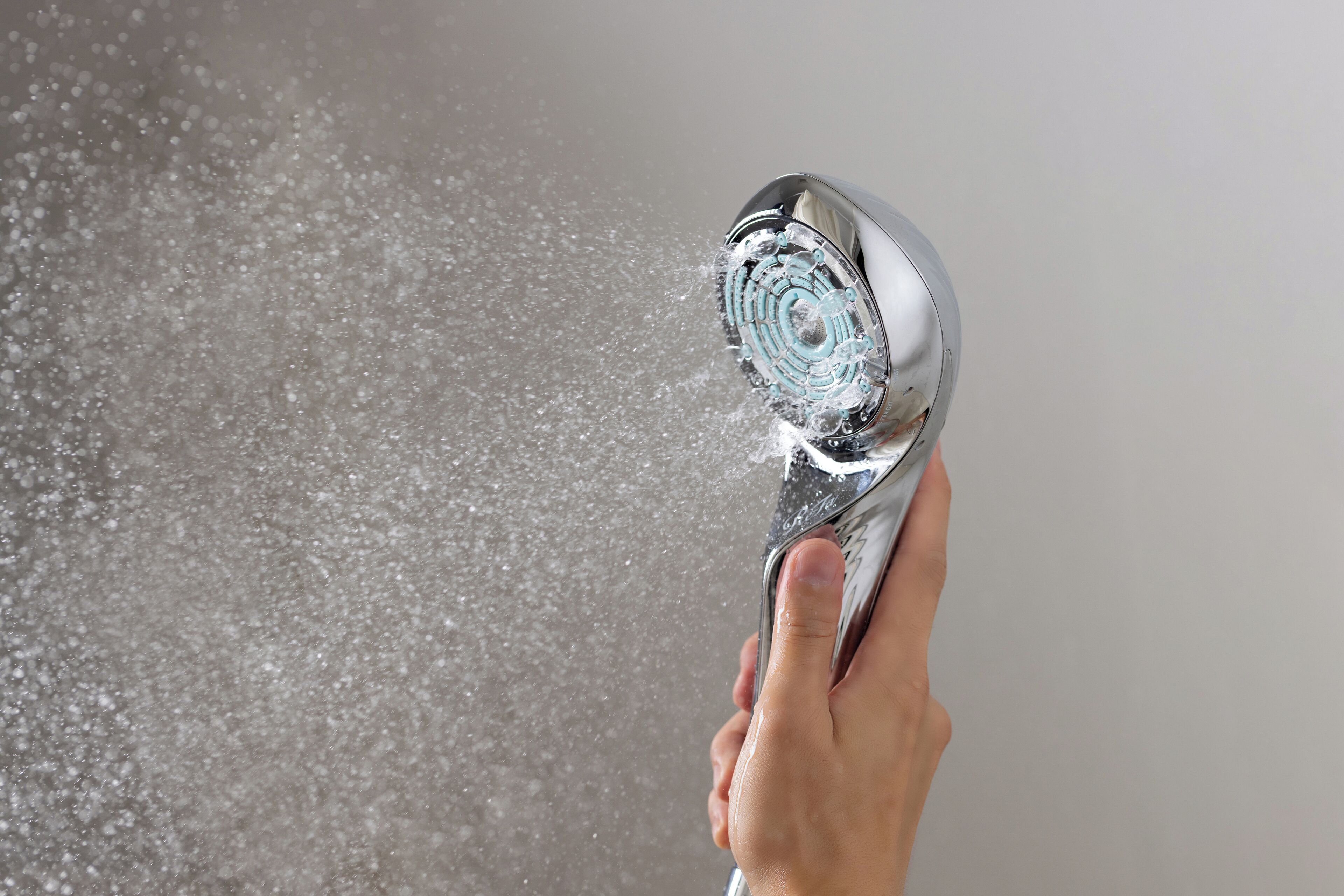 A hand holding a showerhead with water spraying out.