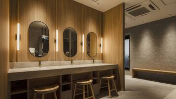 A modern bathroom with wooden paneling, a long vanity with three mirrors, and two stools.
