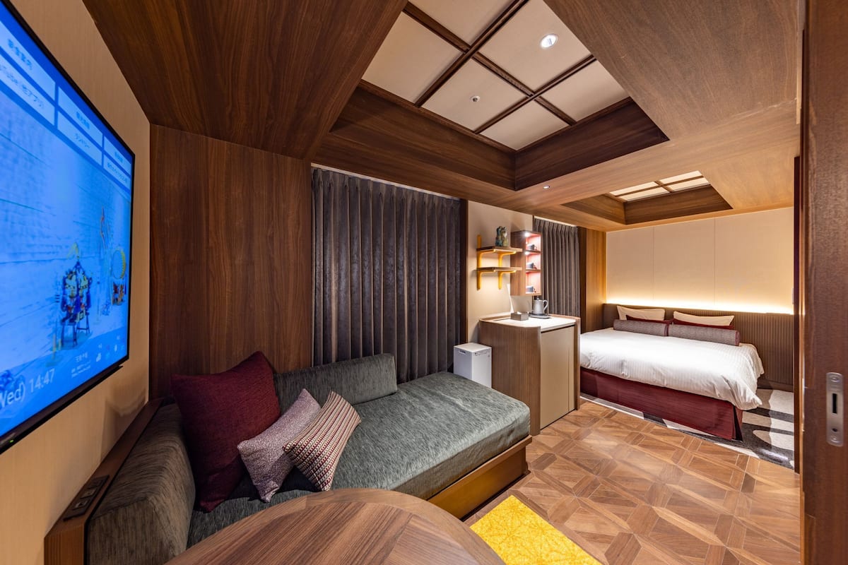 A modern hotel room with a sofa, a bed, a desk, and a TV.