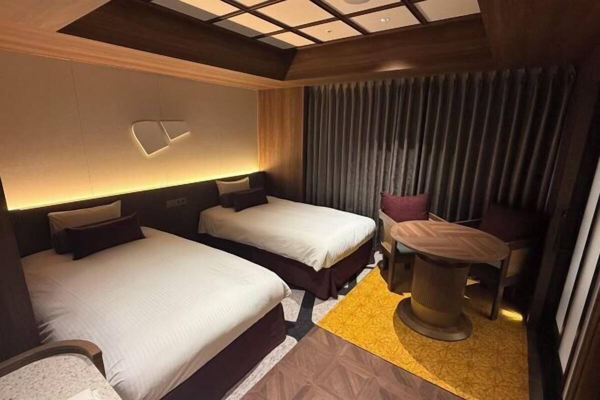 Een hotelkamer met twee bedden, een tafeltje en een gordijn.
