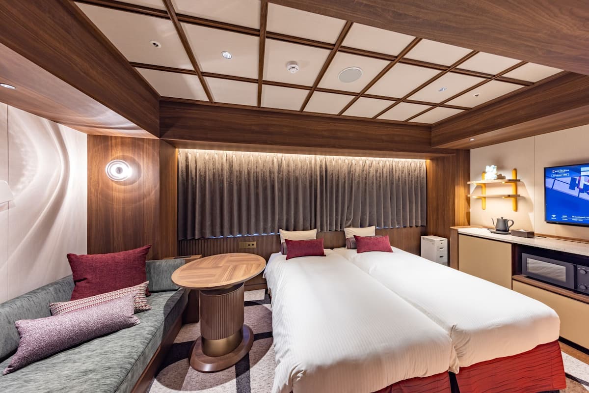 A hotel room with a sofa, two beds, a TV, and a small table.