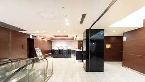 Een moderne hotel lobby met een glazen balustrade, een receptiebalie en een zwarte lift.