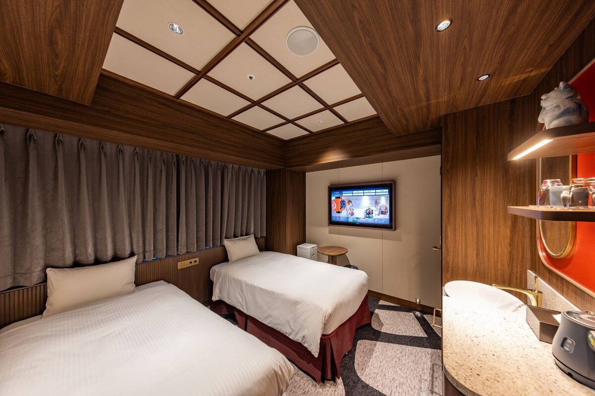 A hotel room with two beds, a television, a small table, and a sink.