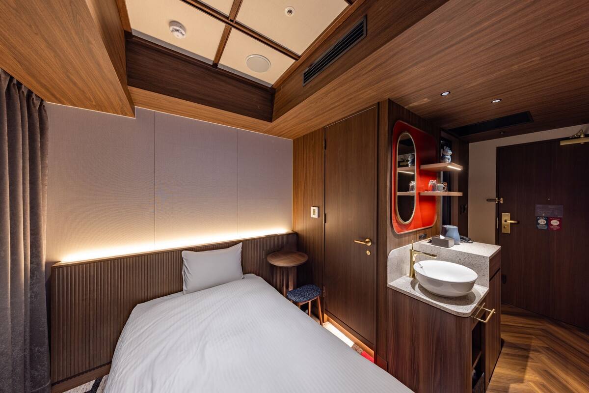 A modern hotel room with a large bed, a small round table, a built-in vanity with a mirror, and a ceiling with recessed lighting.