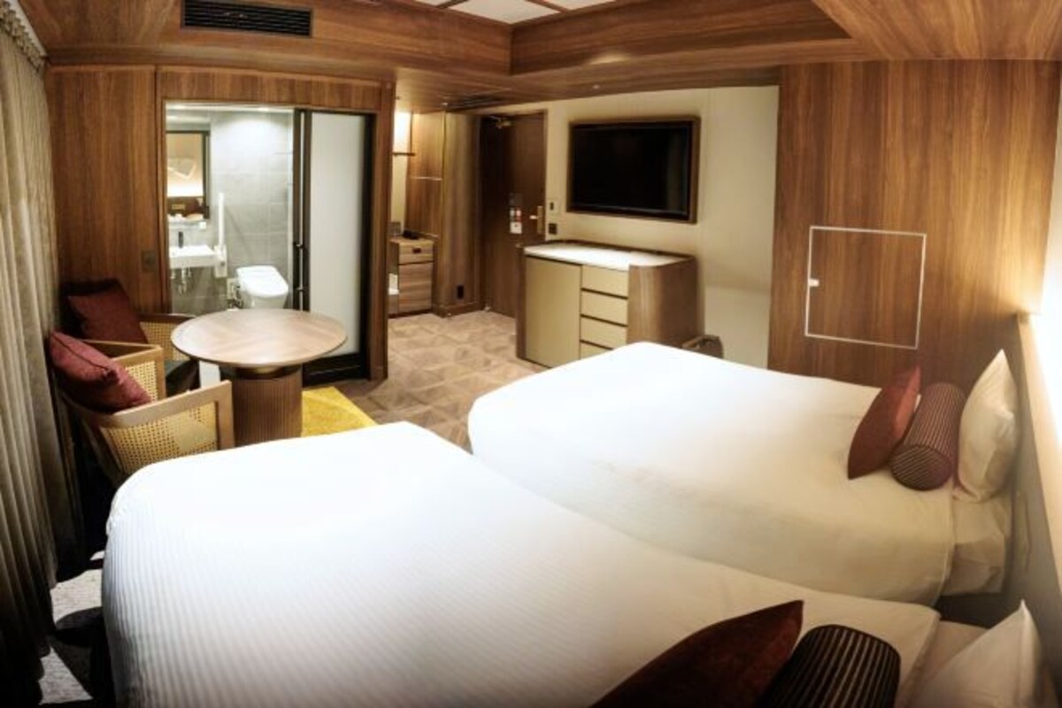 Une chambre d’hôtel avec deux lits, une petite table ronde, un téléviseur et une salle de bain avec un miroir et un lavabo.