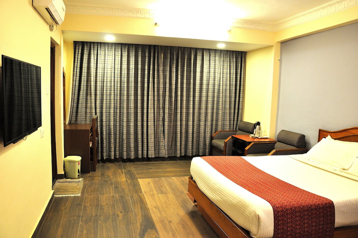 Una habitación de hotel con una cama, un escritorio, una silla, un televisor y una ventana con cortinas.