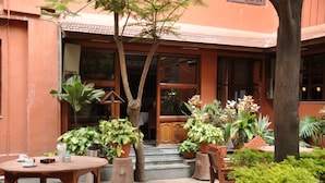 An outdoor seating area with tables and chairs, surrounded by potted plants and trees. - Tibet Guest House (Kathmandu)