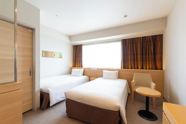 A hotel room with two beds, a small table, a chair, and a wardrobe.