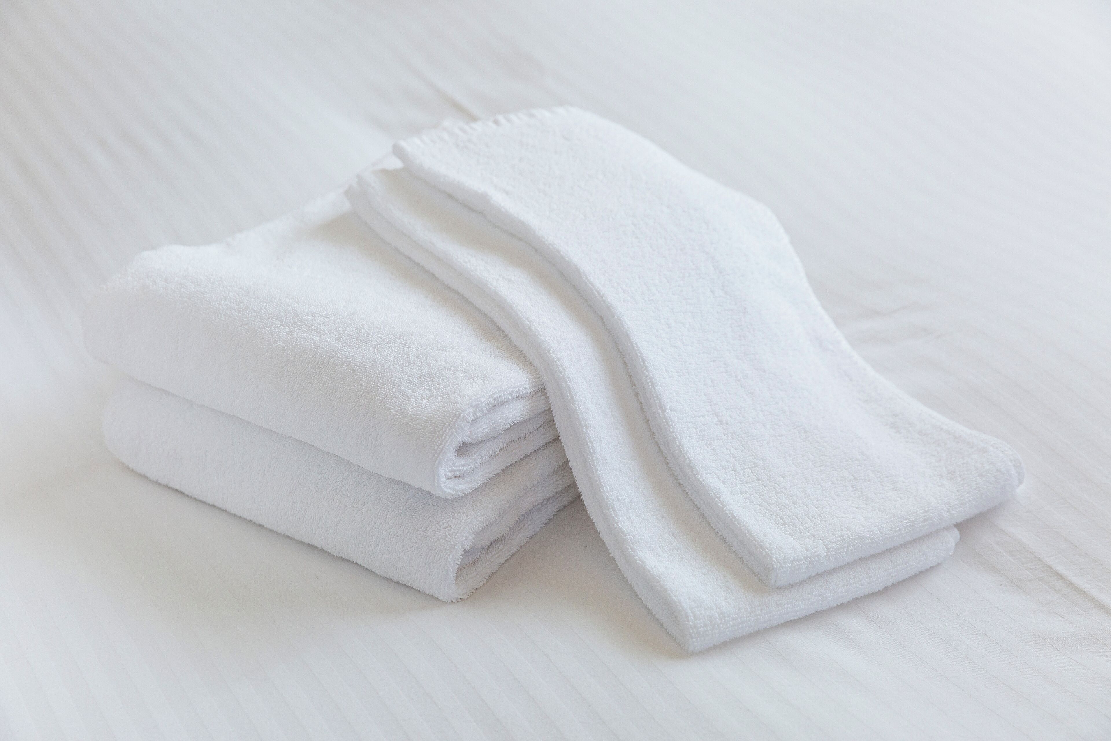 Una pila de toallas blancas sobre una cama blanca con textura suave.
