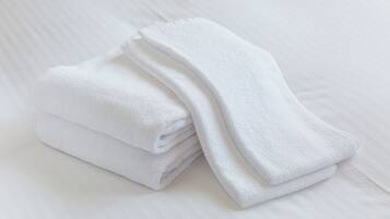 Una pila de toallas blancas sobre una cama blanca con textura suave.