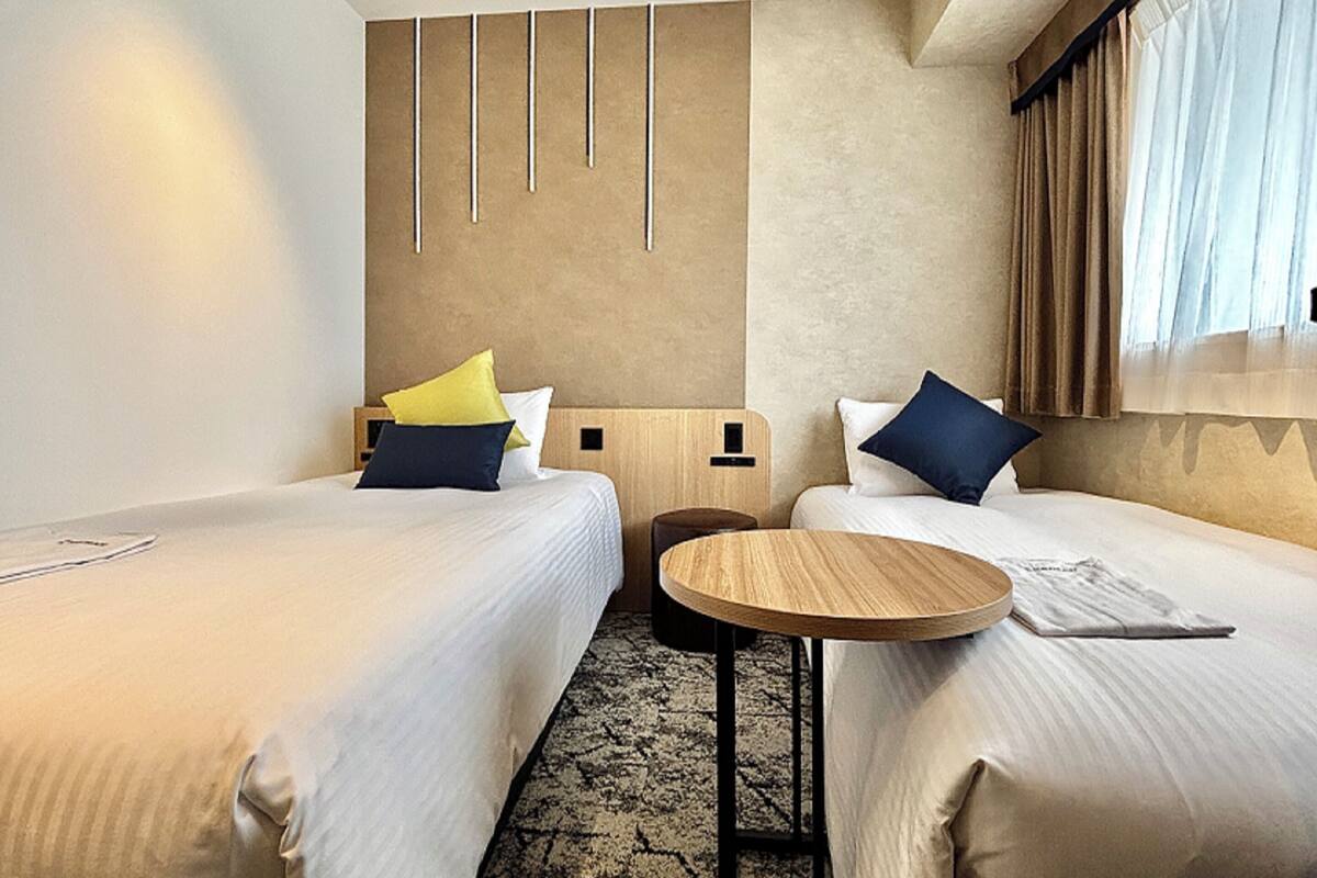 Ein Hotelzimmer mit zwei Betten, einem kleinen runden Tisch und einem Kopfteil mit vertikalen Linien.