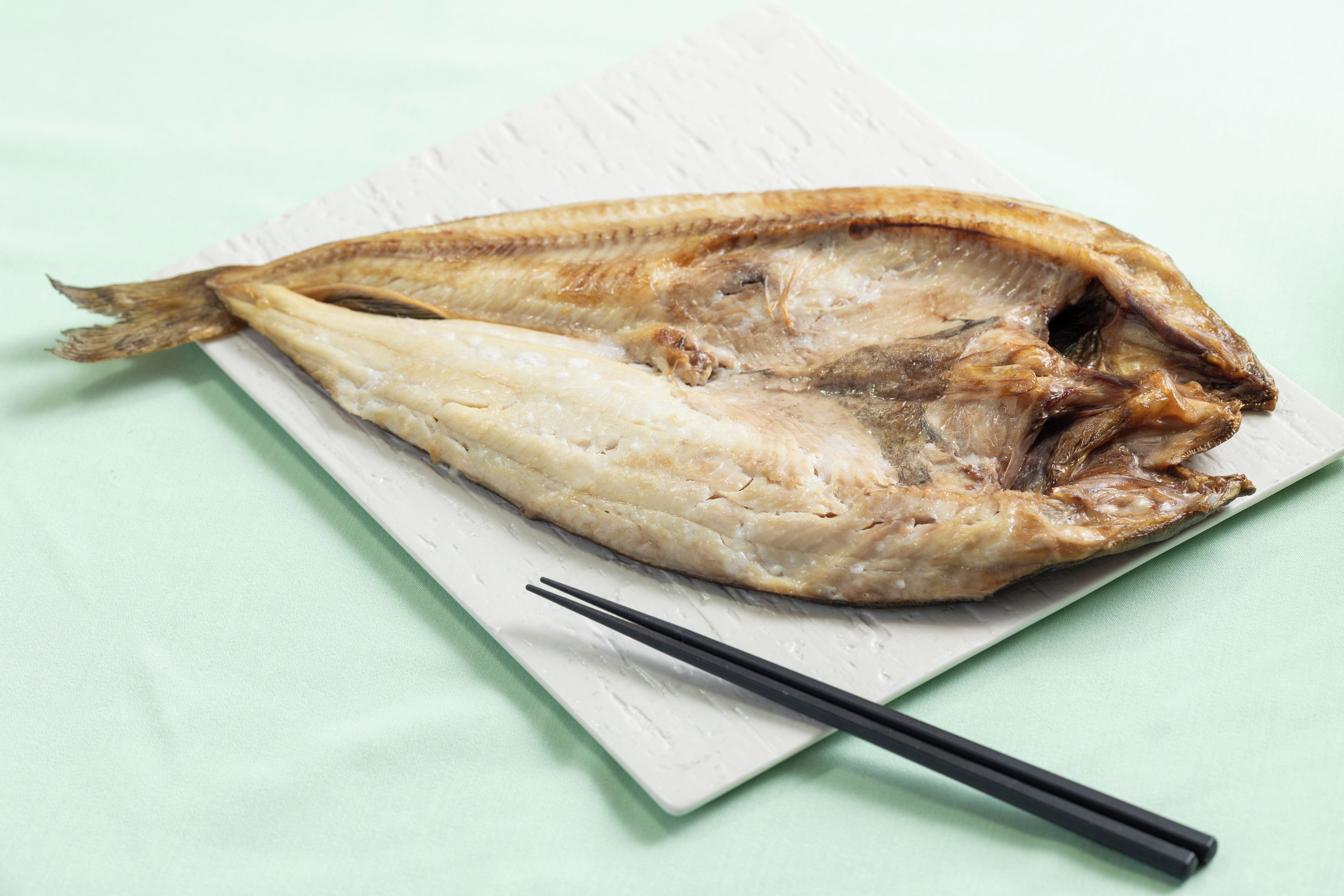 A dried fish on a white plate with chopsticks beside it.