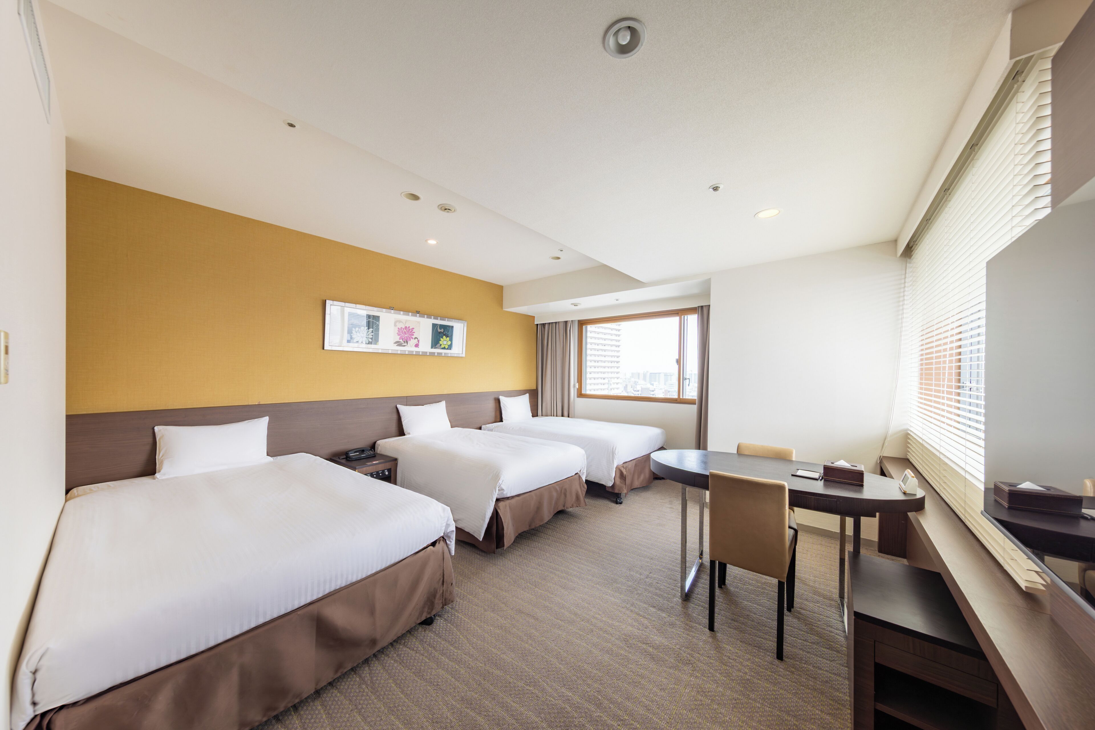 A hotel room with three beds, a desk, and a chair.