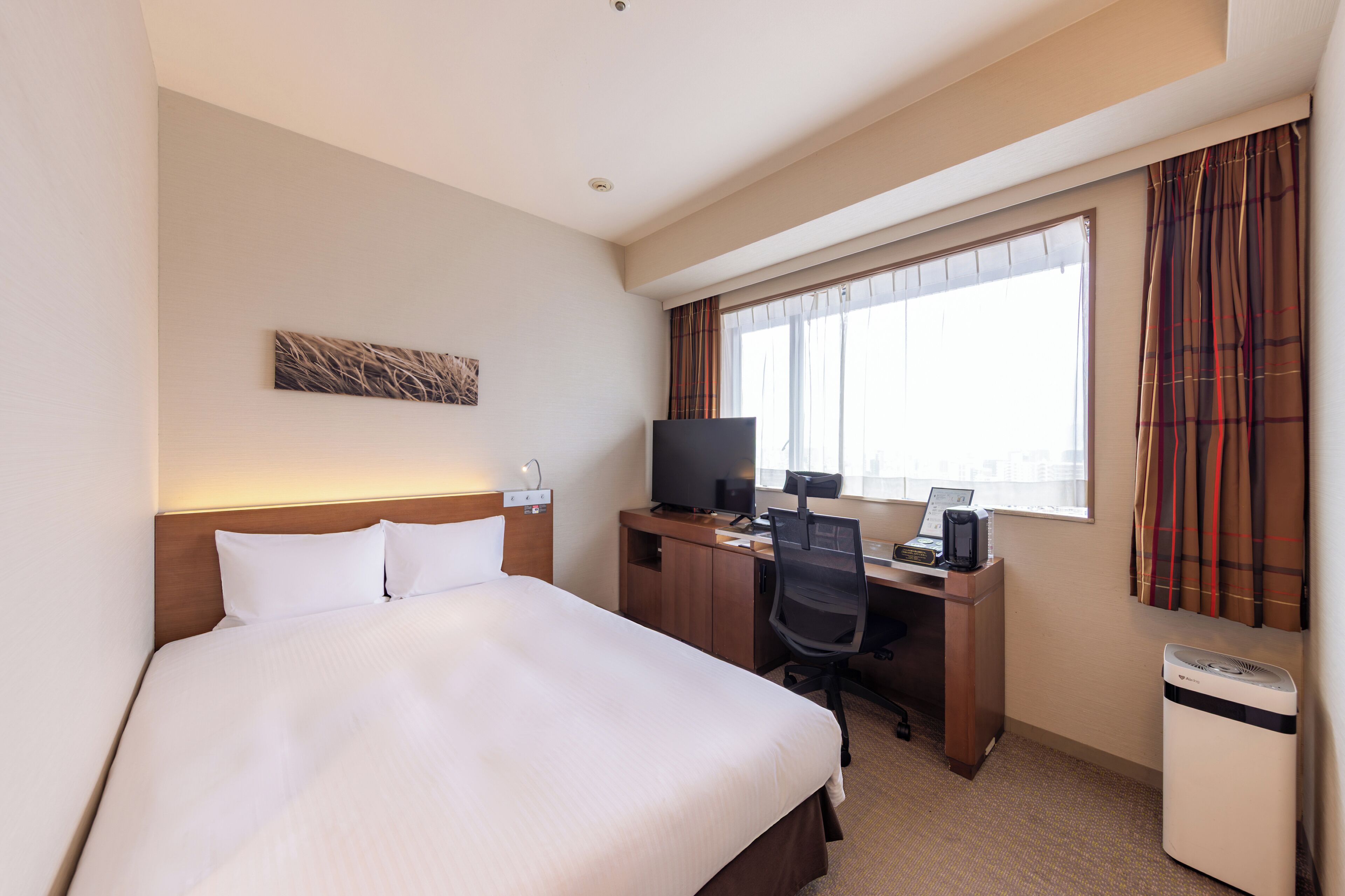 A hotel room with a bed, desk, television, and a window with curtains.