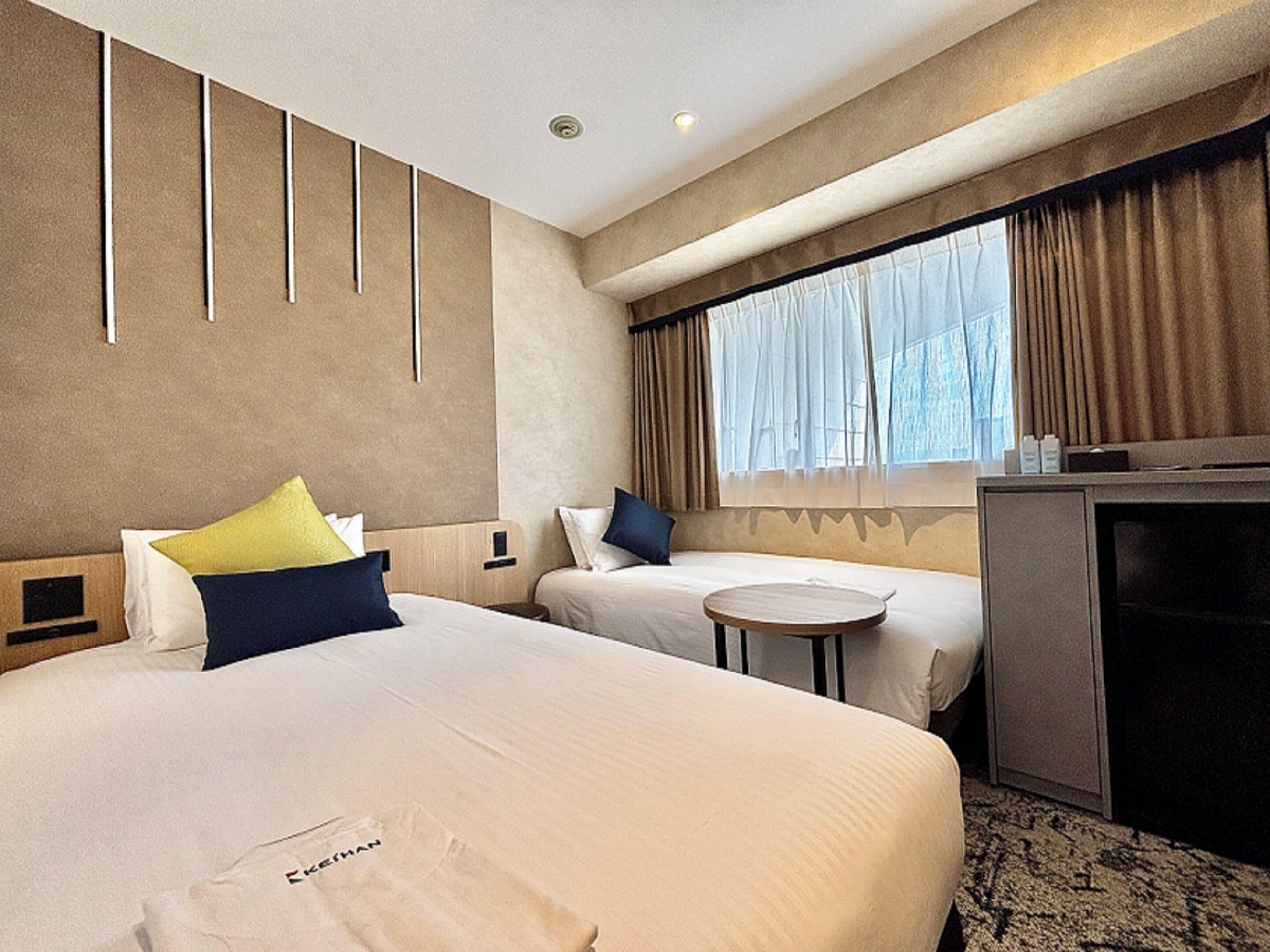 A hotel room with two beds, a desk, and a window with curtains.
