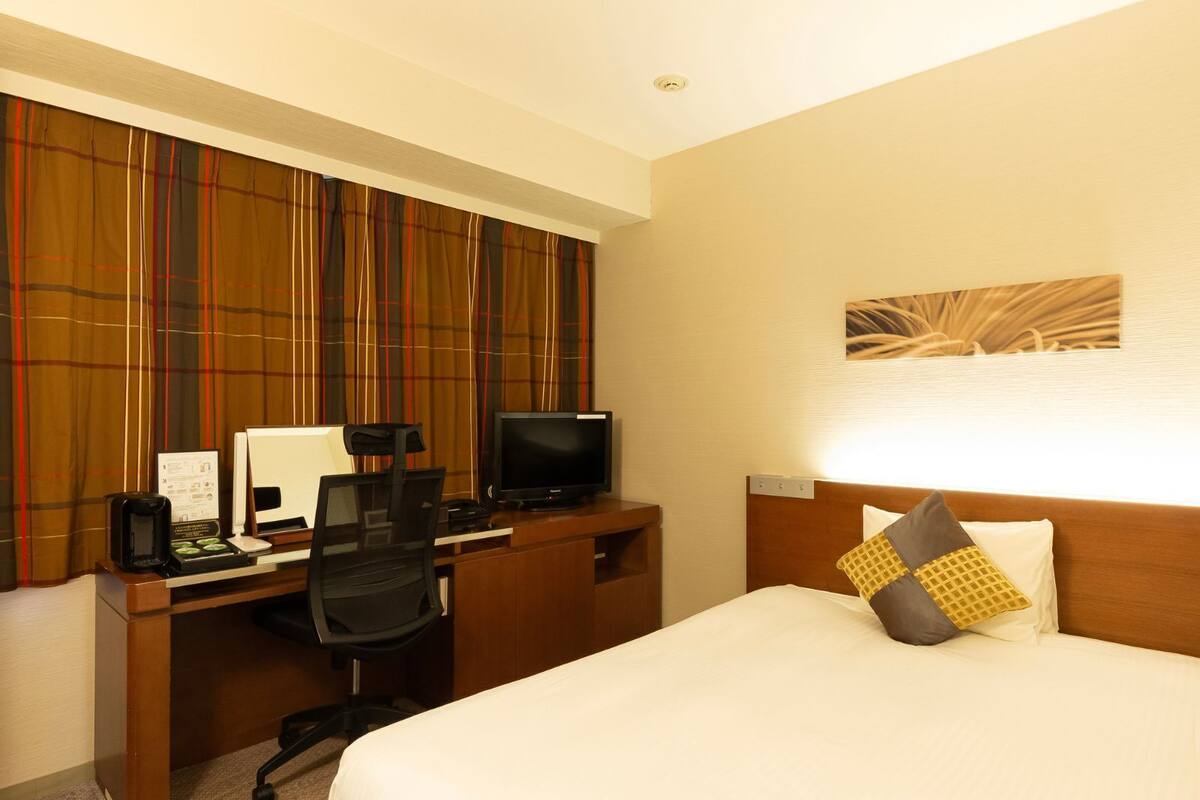 Ein Hotelzimmer mit einem Bett, einem Schreibtisch mit Computer, einem Sessel und einem Fernseher.