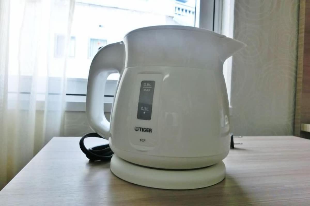 A white electric kettle on a wooden table near a window.