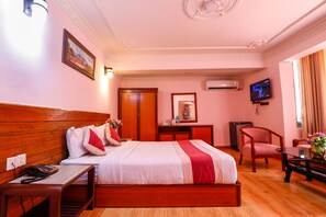 A hotel room with a wooden bed, a desk with a telephone, a chair, a television, and a mirror. - Hotel Blue Horizon (Kathmandu)