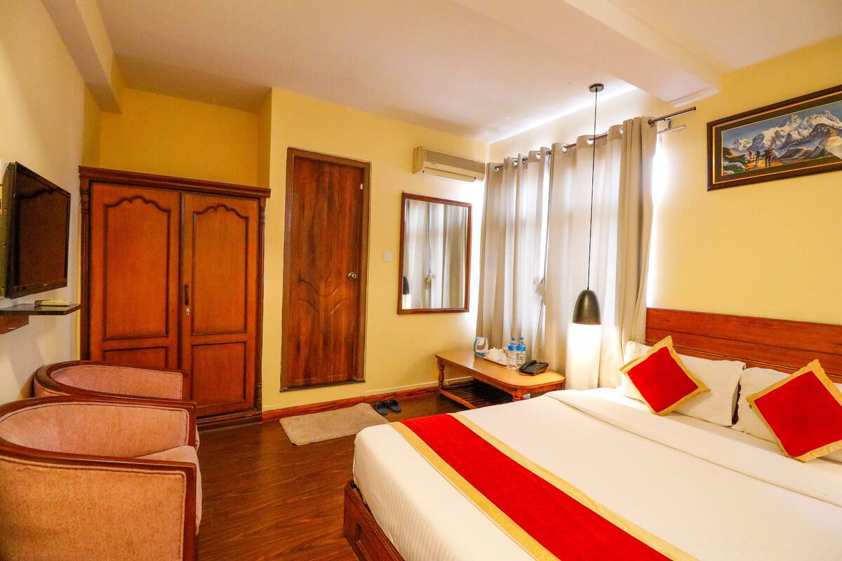 A hotel room with a large bed, wooden wardrobe, a desk, and a chair.