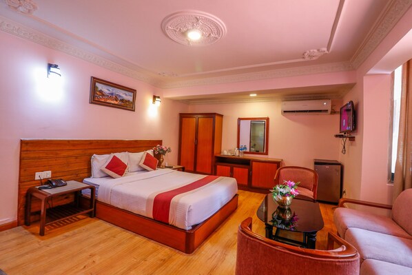 A hotel room with a large bed, a desk, a chair, a small table with flowers, a TV, and a wardrobe. - Hotel Blue Horizon (Kathmandu)