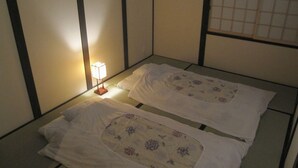 A traditional Japanese room with tatami flooring, two beds with floral bedding, and a bedside table with a lamp. - Kagariya (Kyoto)