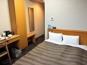 Habitación de hotel con cama, escritorio, silla, cesto de basura y espejo.