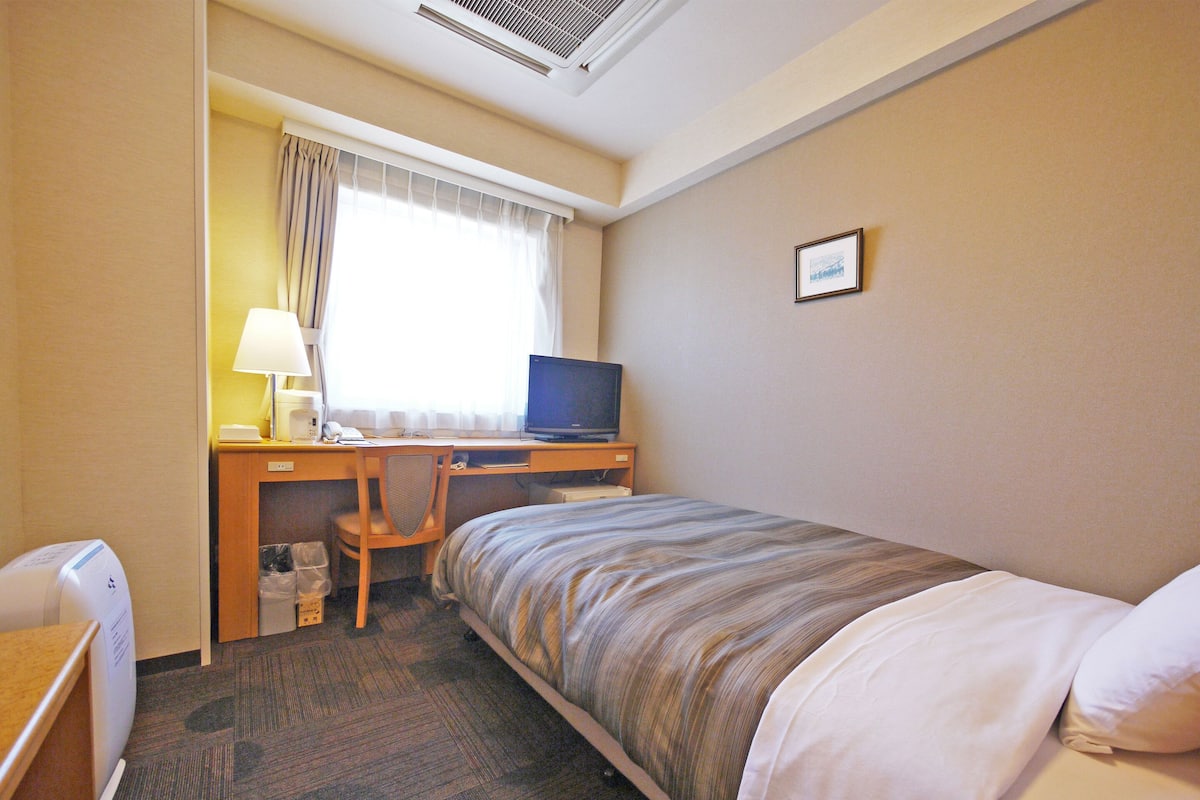 A hotel room with a bed, a desk with a computer, a chair, and a small table.