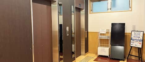 Un vestíbulo de hotel con un mostrador de recepción, un refrigerador y un tablón de anuncios.